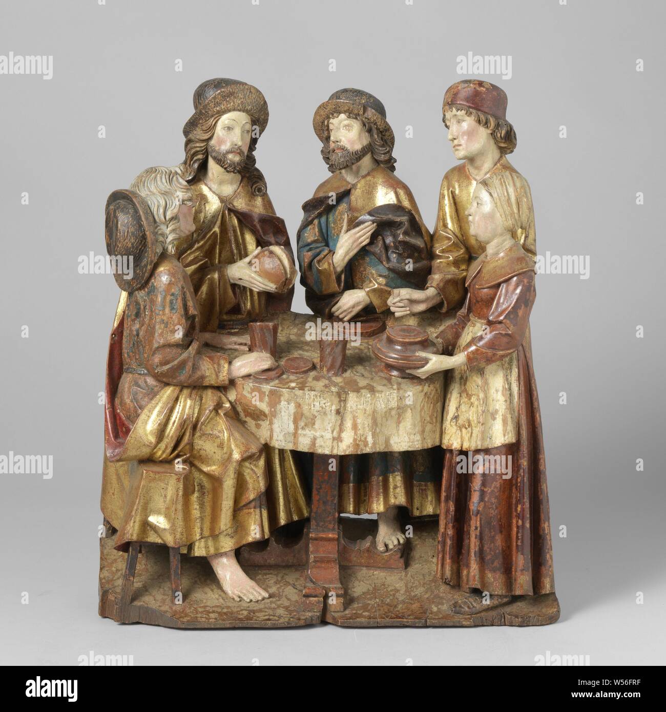 The Supper at Emmaus The Emmaus goers, On an ascending floor behind a set round table there is Christ between the two Emmaus goers, to the right of them are a man and a woman. Christ is pictured the moment He breaks the bread. The stigmata on his hands. The Emmaüsganger, sitting to his left in profile, holds his fingers against a twisted mug and has his left hand next to him on the table. The second Emmaus gaze turns his gaze to Christ, holds up a fold of the mantle with the right hand and pulls a part of it over the lap with the left. The standing man points with his left hand in Stock Photo