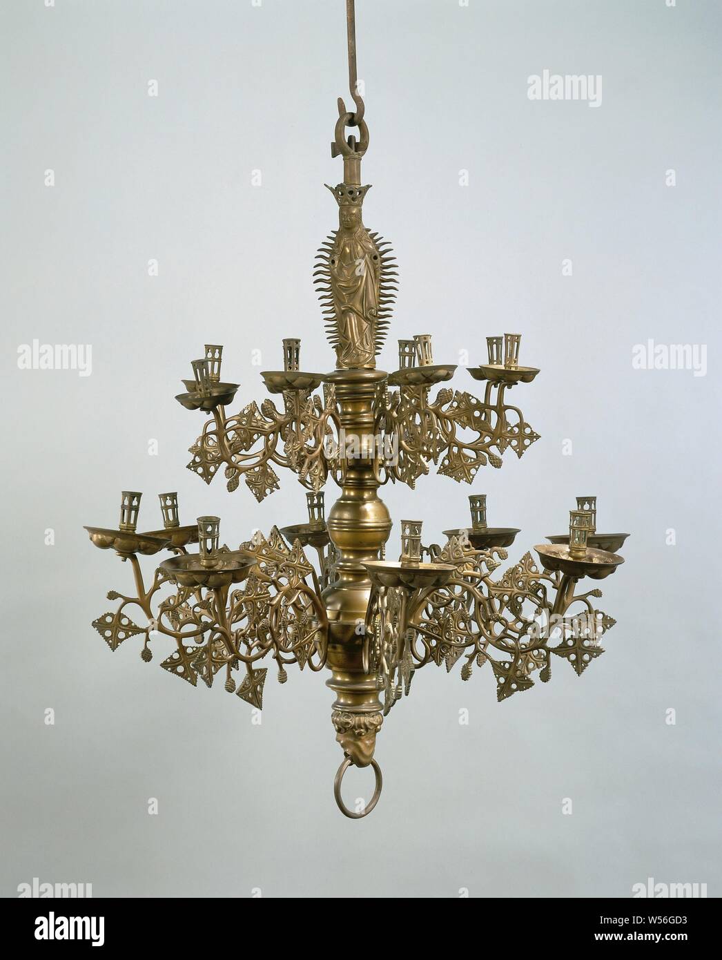 Candle crown, The object consists of an iron rod and an iron split pin and the following cast parts of yellow copper: the hanging ring, the Maria figure with the crown riveted to her head, the trunk, the lion's head with the pull ring. The hanging ring turns into an octagonal pipe piece at the bottom. The Virgin Mary figure placed on the crescent moon is surrounded by a halo. Her dress is decorated with punched star motifs, the hem of the cloak is punched. The hair reaches from the back to the waist. Her crown is composed of five leaves. The trunk is shaped in such a way that two spheres and a Stock Photo