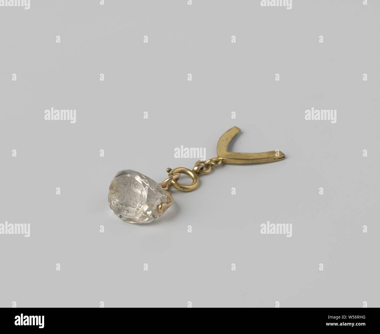 Cachet with the coat of arms of Pieter Labbert (?) Schmidt, On the one side a rock crystal is attached to the golden dangle with eyelet and bearing ring. The crystal has three oval sides, one of which is decorated with a coat of arms. A copper pendant is attached to the other side of the pendant, consisting of a round closure with a carrying eye, two links and a holder with a carrying eye. The holder is empty and has the shape of a gothic arch, Pieter Labbert Schmidt, Colombo, 1700 - 1750, gold (metal), copper (metal), grinding, h 1.3 cm × w 1.1 cm Stock Photo