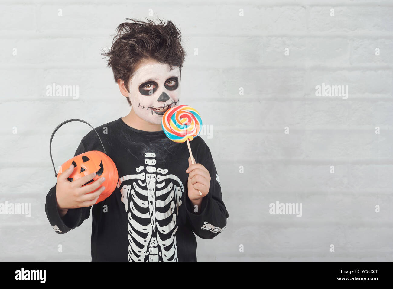 Happy Halloween.funny child in a skeleton costume eating lollipop in halloween against  brick background Stock Photo