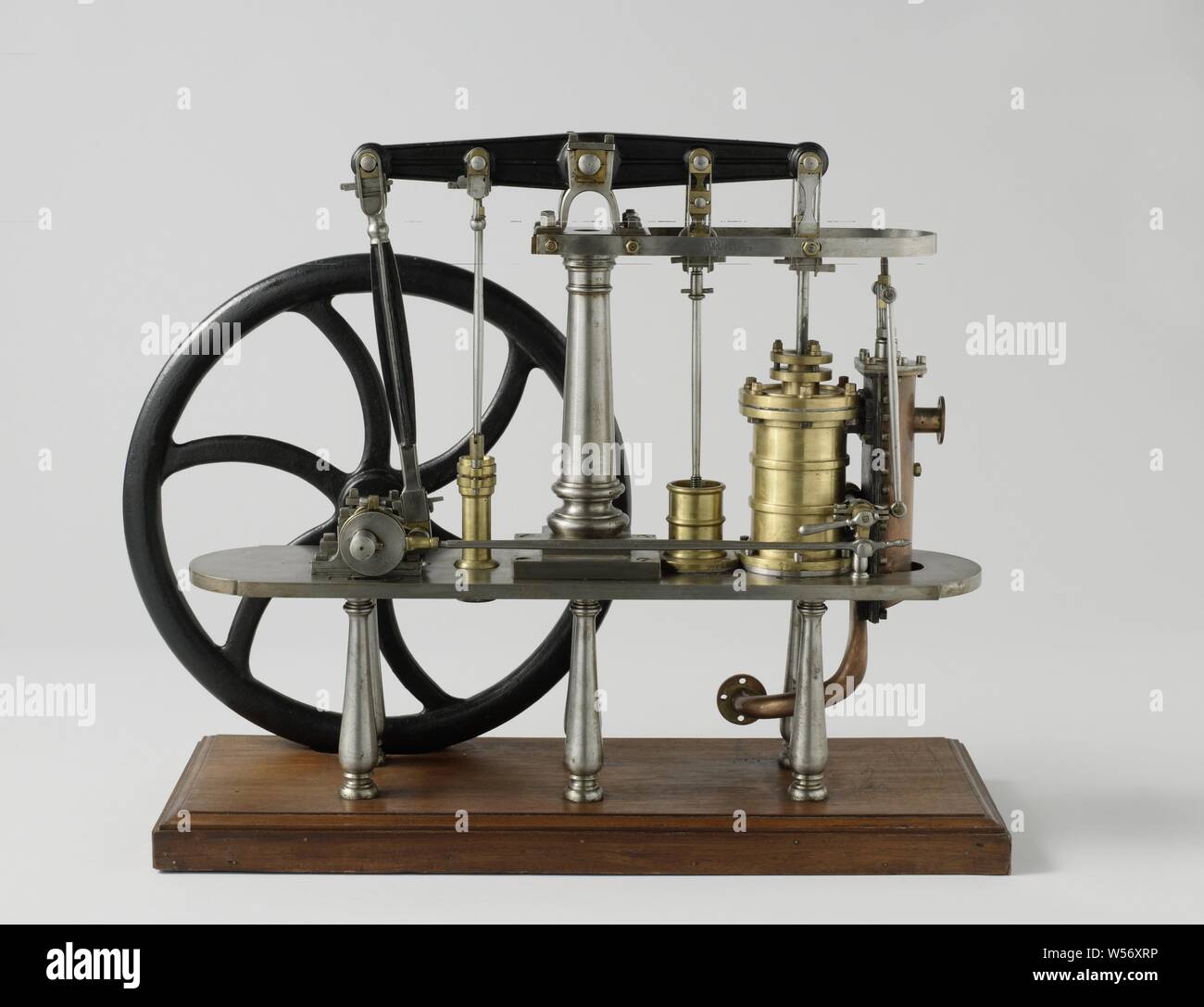 Model of a Double-Acting Beam Engine, Model of a double-acting land-based steam engine, on a wooden ground board. The model has a balance and flywheel, but no condenser. The piston drives the balance, which in turn drives the air pump, the cold water pump of the condenser and the crankshaft. The flywheel is mounted on the crankshaft and on the other side an eccentric with a long drive rod, which drives the steam slide on the other side of the machine. The steam valve has two inputs on the cylinder. The air pump seal is missing. Scale 1:20 (derived)., H.W. Fricke (mentioned on object), 1840 Stock Photo