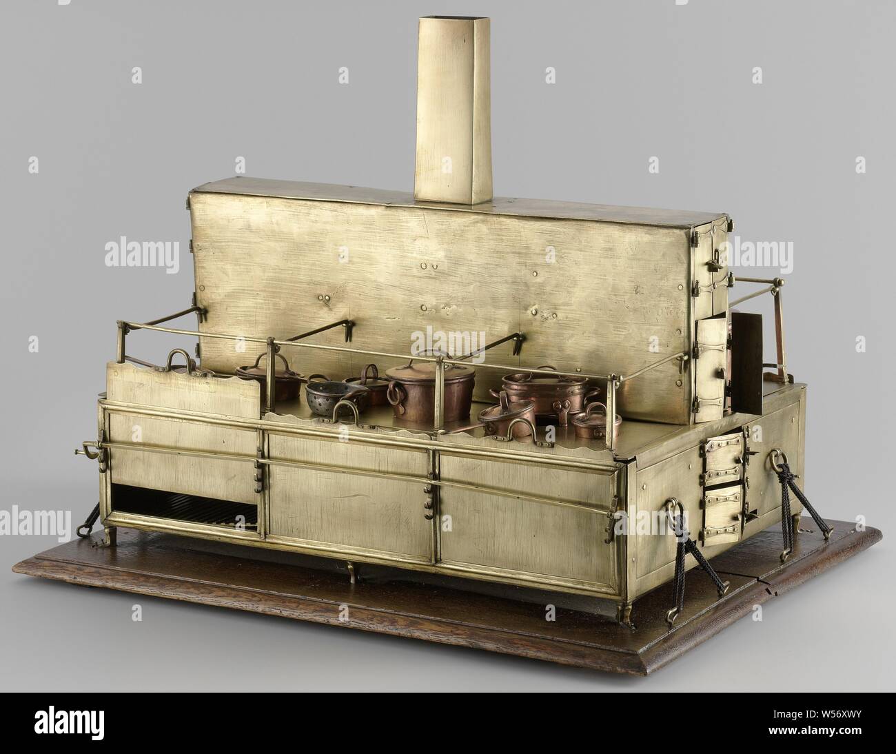 Model of a ship's galley, Model of a Ship's Galley, Model of a ship galley on a floorboard. It is a low rectangular cupboard with a raised smoke box in the middle over the entire length, on which the chimney stands. The whole is bolted on deck with small legs. The two sides on each side of the smoke cabinet are identical except for the hot plates: they consist of three fireplaces with grilles and doors that slide vertically. The hot plates are simple metal plates with round holes for the pans and surrounded by a railing. Between the two rows of fireplaces under the smoking cabinet, bread ovens Stock Photo