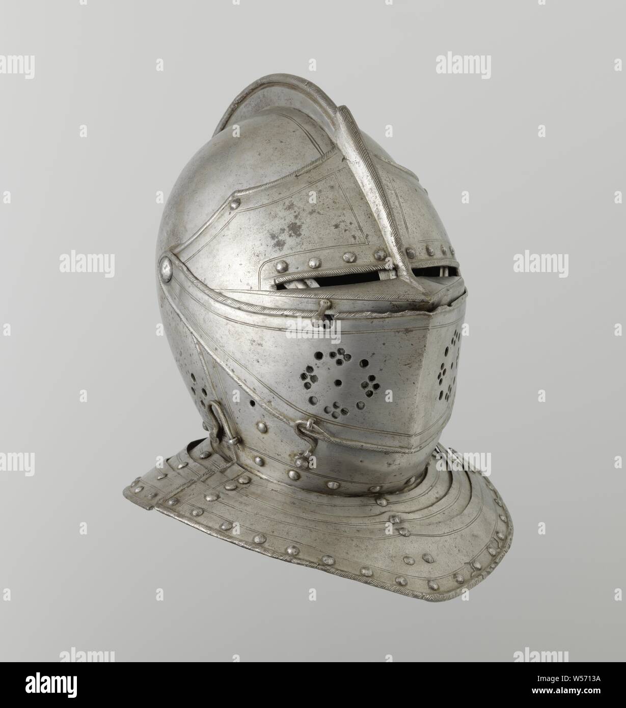 Equestrian helmet made of iron, Equestrian helmet, iron, blank, the helmet ball composed of two halves. Long low comb with cabled edge that ends under the iron plume tube. The articulated neck plate is riveted to the helmet ball and has a cabled flange edge. Closed from the front with three plates, folding up at a common point. The chin plate is riveted to the articulated neck plate and the helmet ball and has a cabled edge. On the left side of the chin plate a hook that can be attached to the lower visor. Parallel to the edge decoration lines with flattened rivets underneath. The face plate Stock Photo