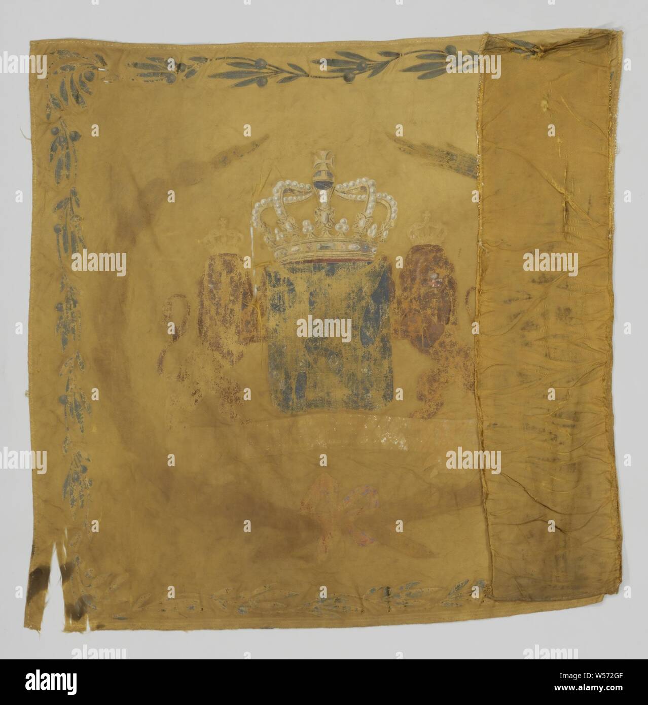 Fragment of yellow cream-colored banner with gold frills. on the front a crowned decorative W, including the inscription: DEPARTMENT OF KURASSIERS NO 1, Fragment of yellow cream-colored banner with gold frills. On the front a crowned decorative W, along the sides green branches with orange berries. On the parade side the crowned weapon of the kingdom, with banderole on which the weapon saying: JE MAINTIENDRAI, held by two crowned looking lions, this whole is surrounded by two raised laurel branches, which are held together at the bottom by a pink bow, along the silk green branches with orange Stock Photo