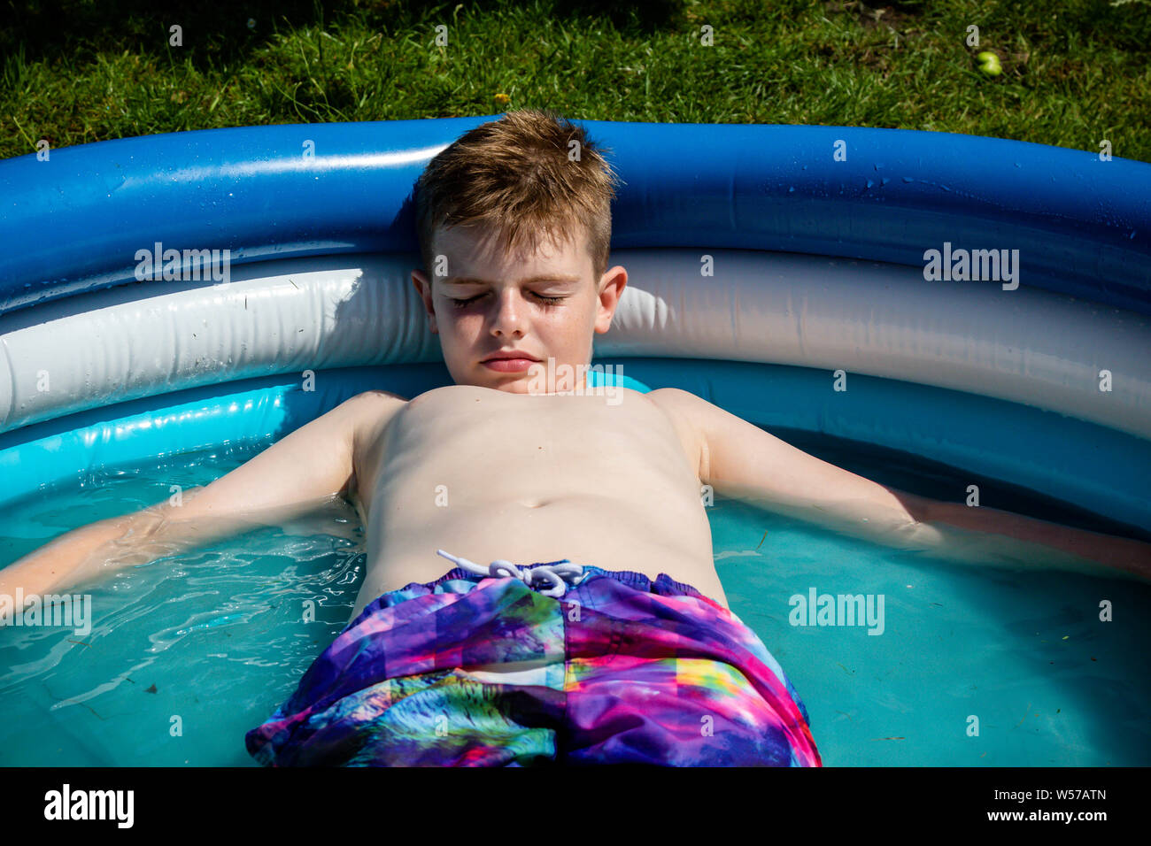 Shirtless preteen caucasian boy laying in a paddling pool Stock Photo