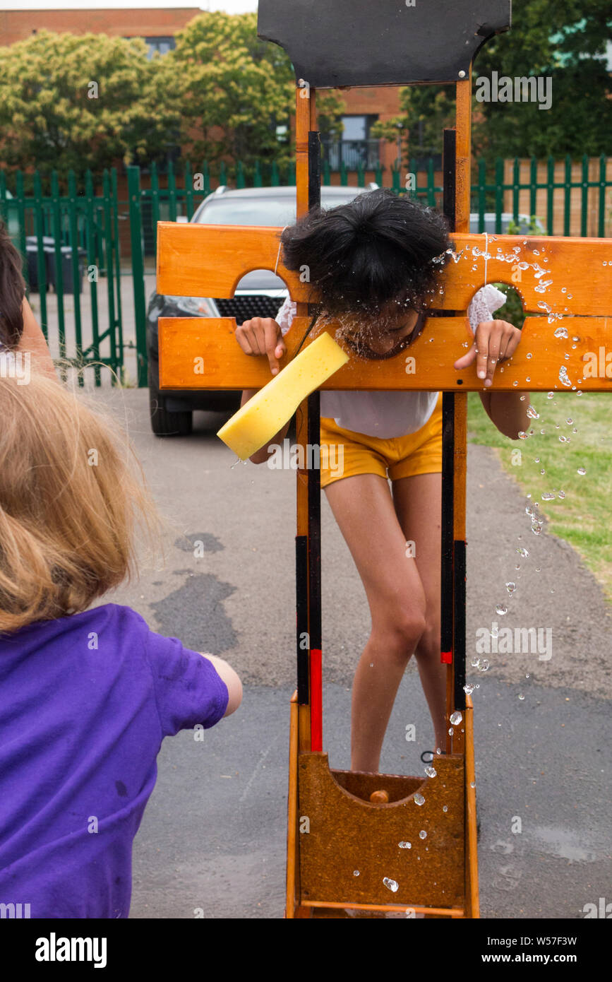 A young child throws a wet sponge at another kid held in mock stocks to raise money for charity at a school fair fête. (111) Stock Photo