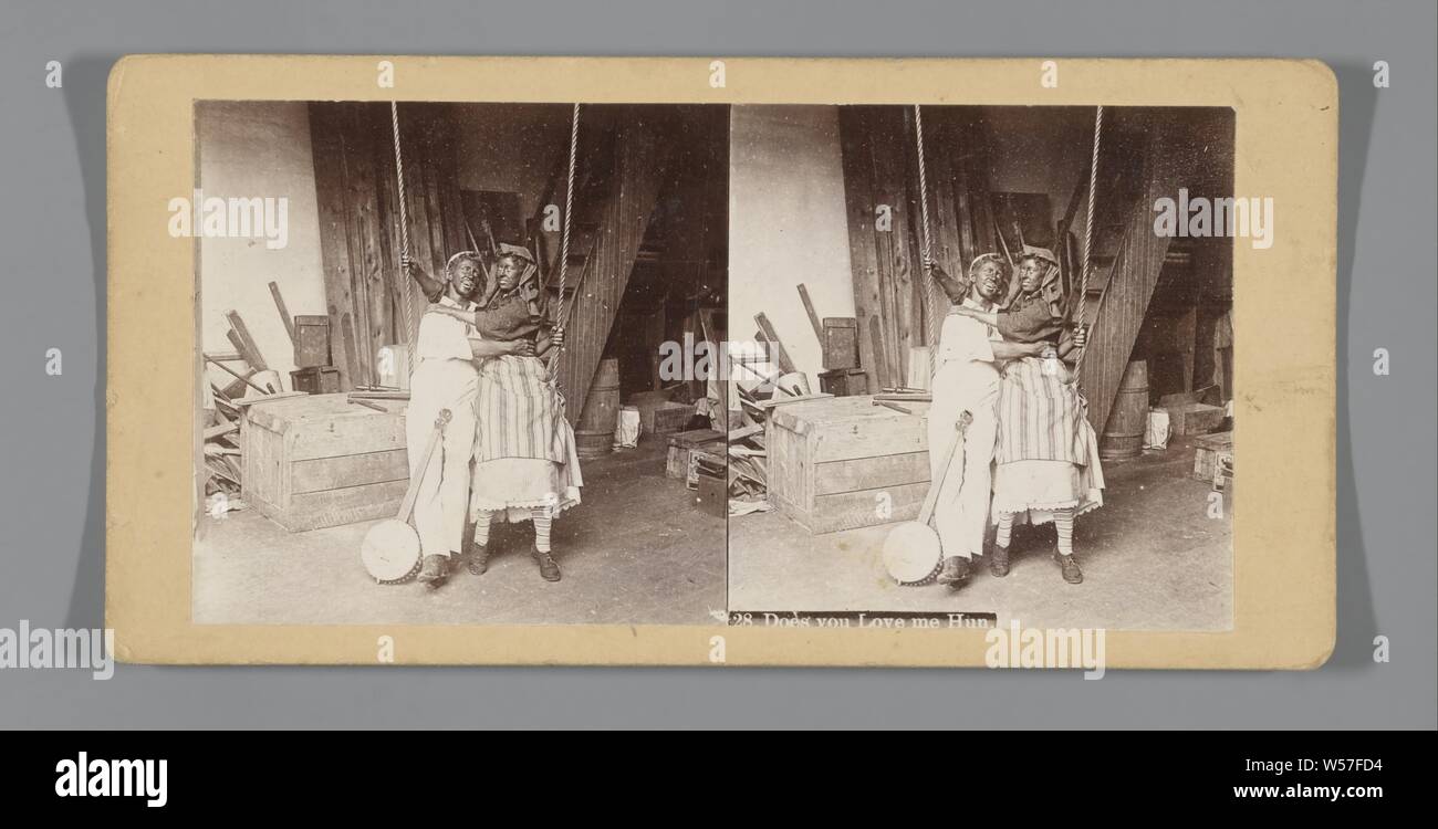 Couple with black painted faces on a swing, Does you Love me Hun (title on object), laughing, painting of body or face, swing, anonymous, The Hague, c. 1890 - c. 1920, photographic paper, cardboard, h 88 mm × w 177 mm Stock Photo
