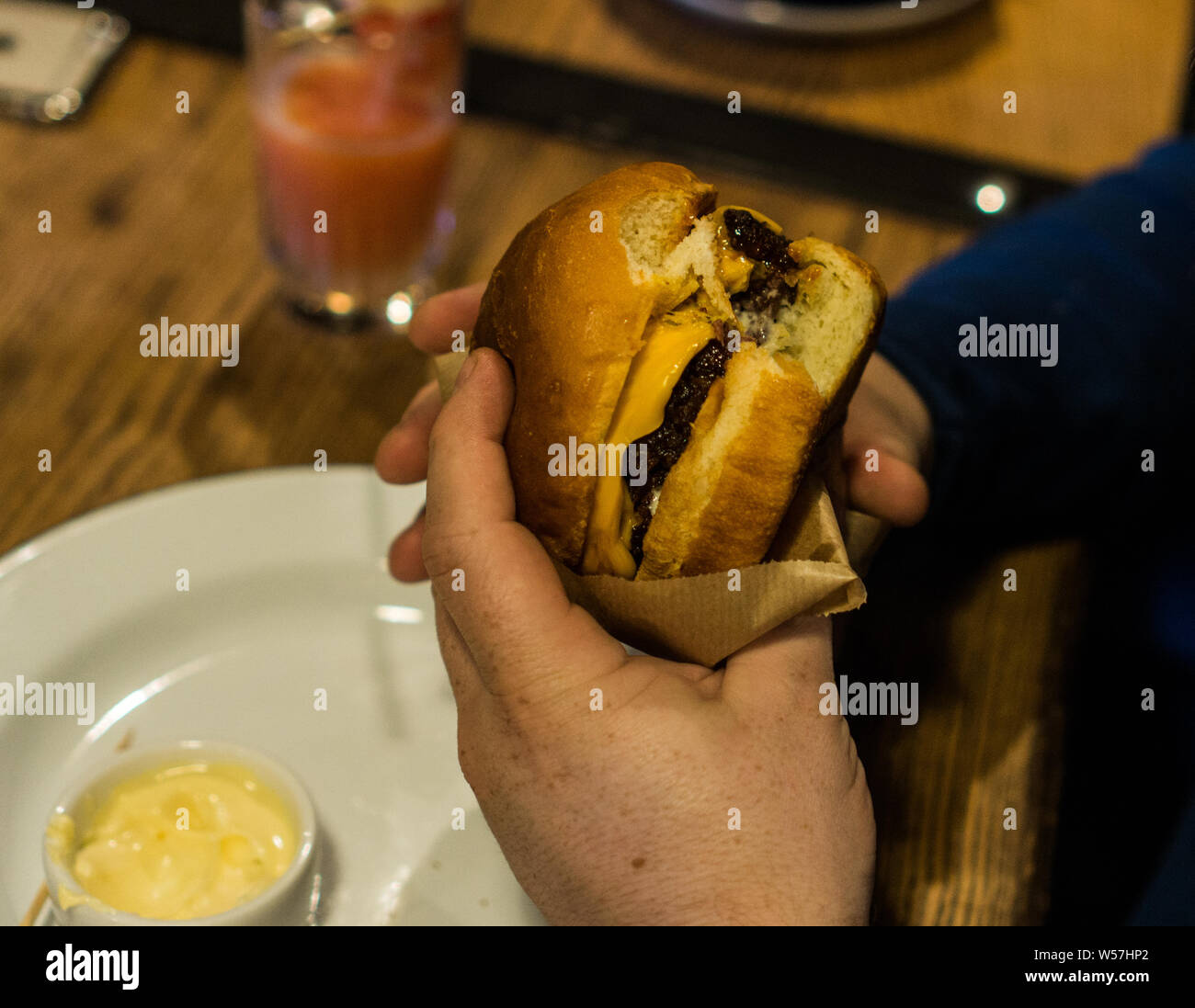 Young man's hands are holding a bitten hamburger in a fast food restaurant. Stock Photo