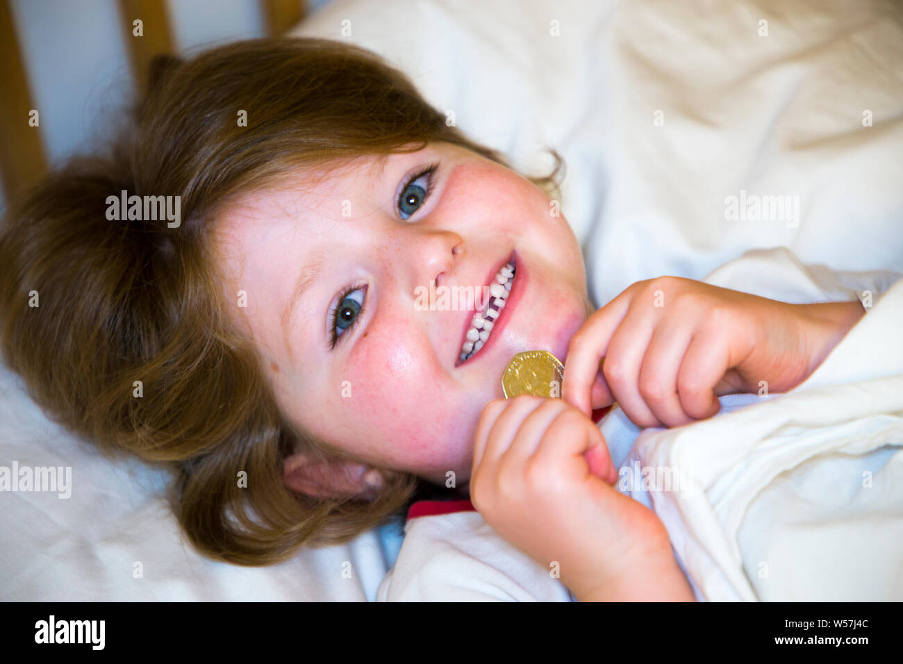 Young girl smiling to reveal a missing front tooth / teeth tooth, whilst holding a 50p / fifty
