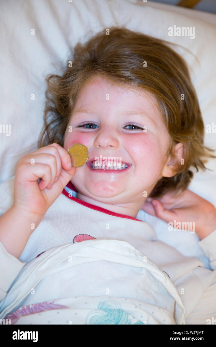Young girl smiling to reveal a missing front tooth / teeth tooth, whilst holding a 50p / fifty