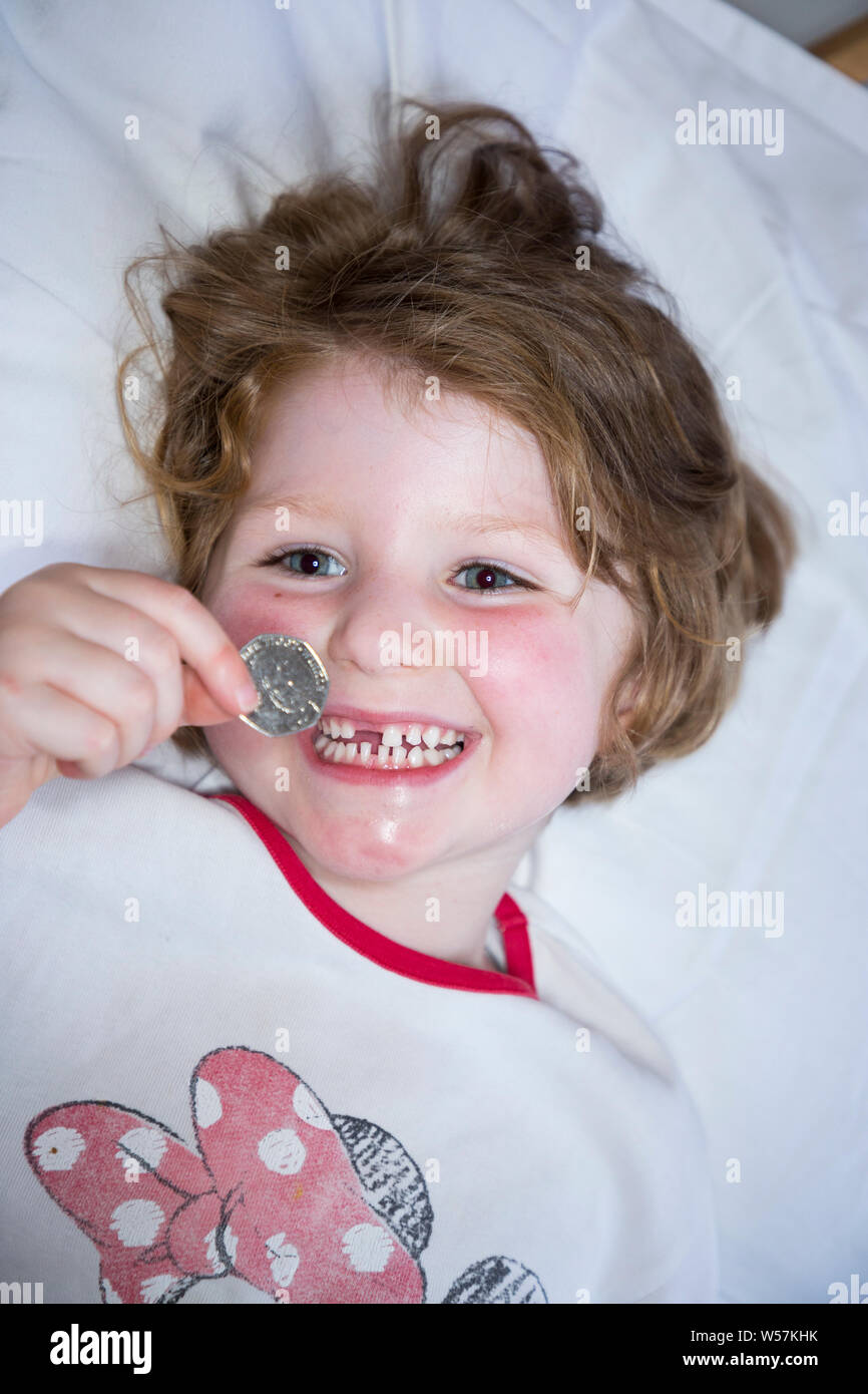 Young girl smiling to reveal a missing front tooth / teeth tooth, whilst holding a 50p / fifty  pence coin in which arrived from the tooth fairy under her pillow. UK (111) Stock Photo