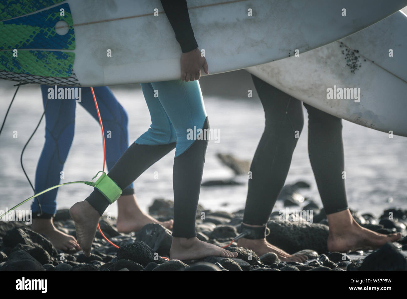 Close up view of three surfer at the beach with board walking barefoot. Close-up view of young legs of sportive men at the beach. Group of young boy p Stock Photo
