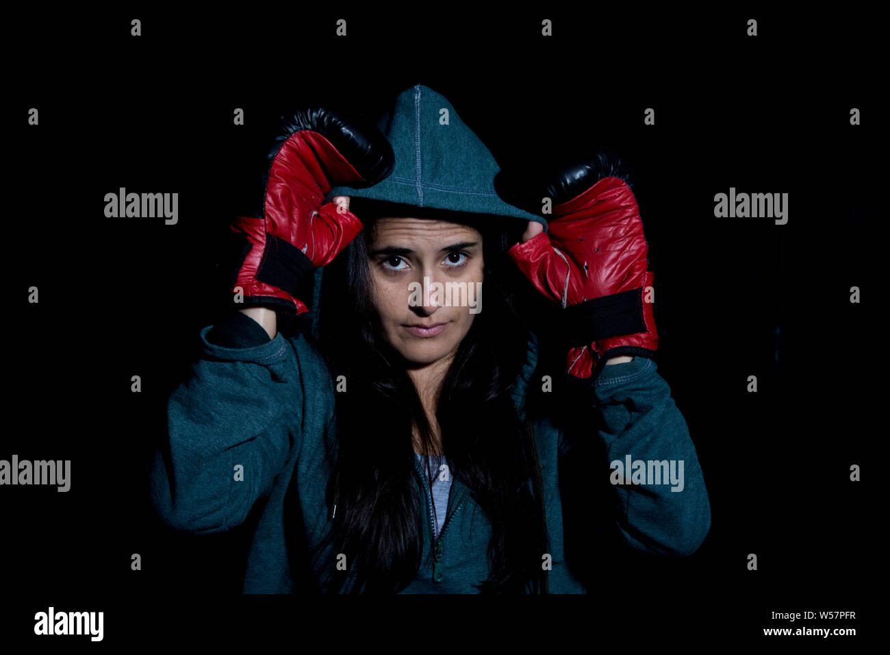 Portrait of young woman exercising boxing in the gym with red gloves on black background Stock Photo
