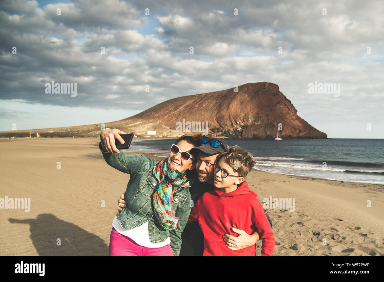 Dad mom with son taking selfie smiling and happy at the beach near the ocean. Parents with child on holiday making pictures for memories of an exotic Stock Photo