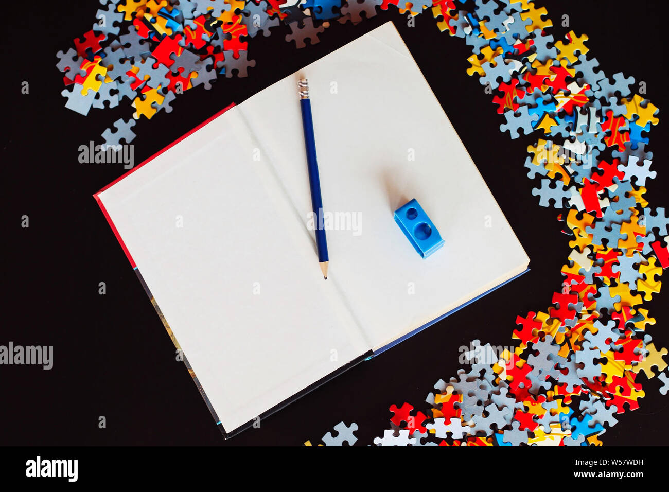 Blank book with pencil and sharpeners next to puzzle pieces. Stock Photo