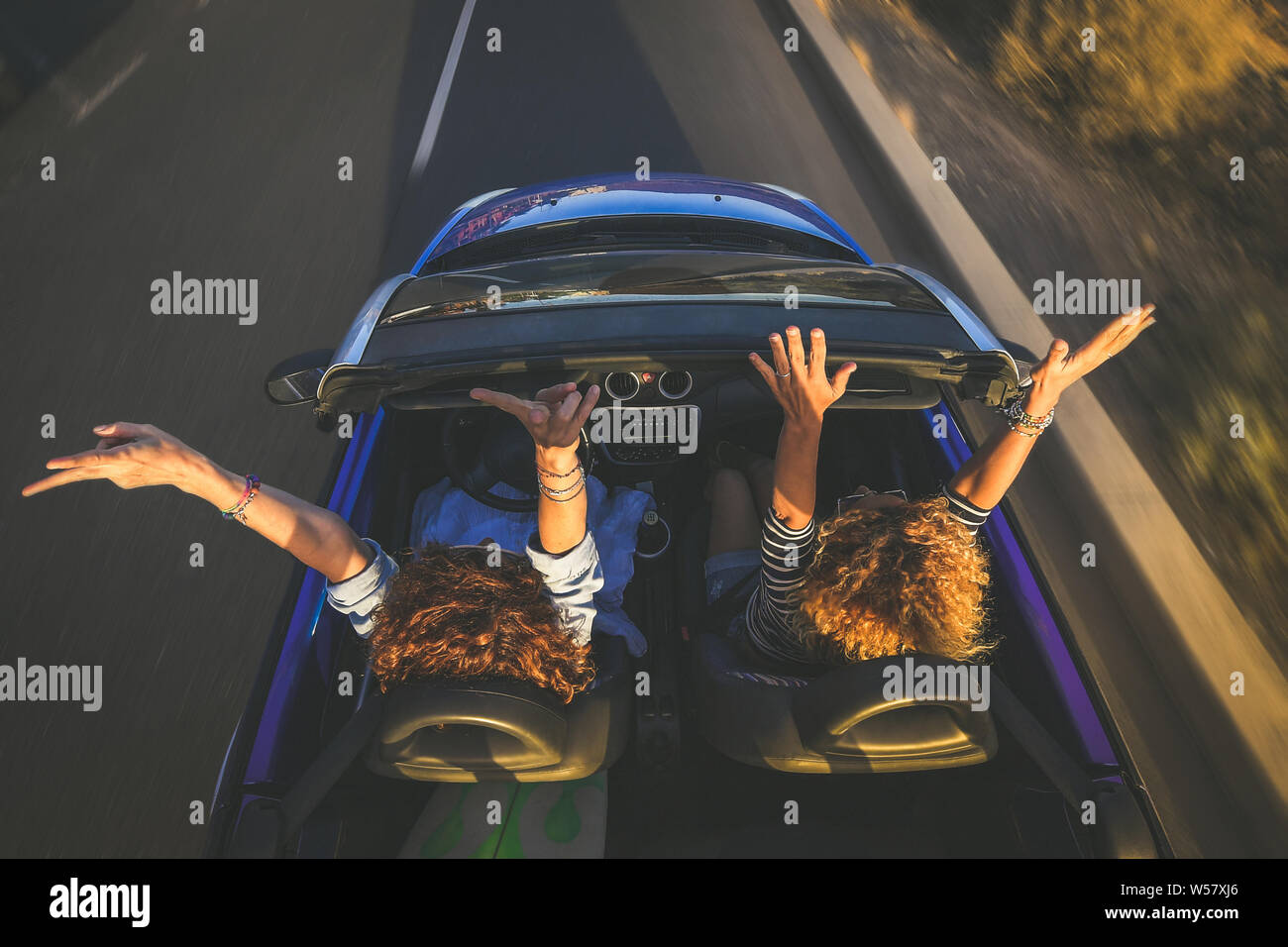 Top view a pair of euphoric women in a convertible car twisting and waving. Two curly girls on vacation having fun driving the auto, laughing happily Stock Photo