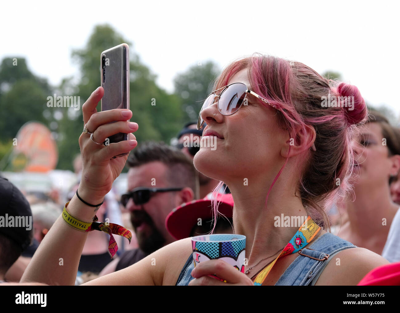 Lulworth, Dorset, July 26th 2019. Woman with dyed red hair in crowd watching acts on stage through her phone, Lulworth, Dorset UK Credit: Dawn Fletcher-Park/Alamy Live News Stock Photo