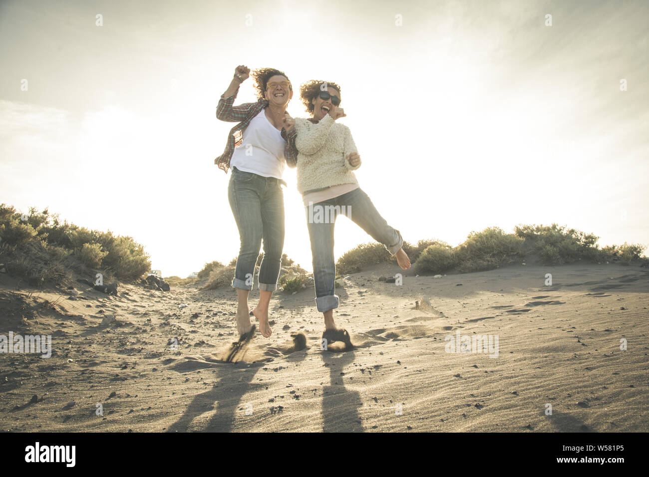 Friendship, summer vacation, freedom, happiness and people concept - two happy female middle age friends dancing and jumping on beach. Full-length sho Stock Photo