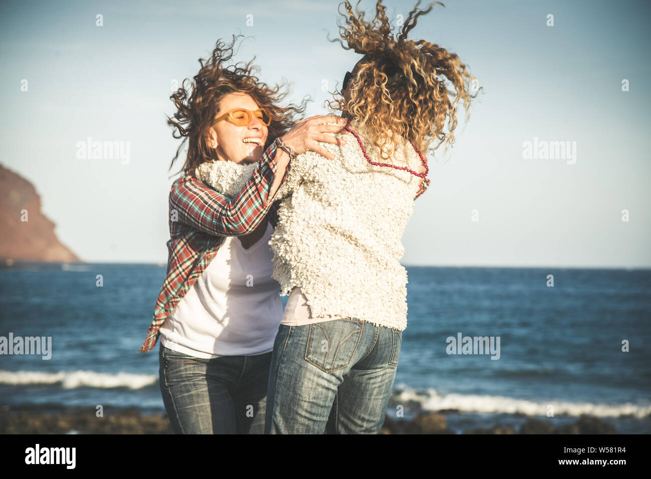 Friendship, summer vacation, freedom, happiness people concept - two happy female middle age friends they hug each other, dancing jumping beach. Full- Stock Photo