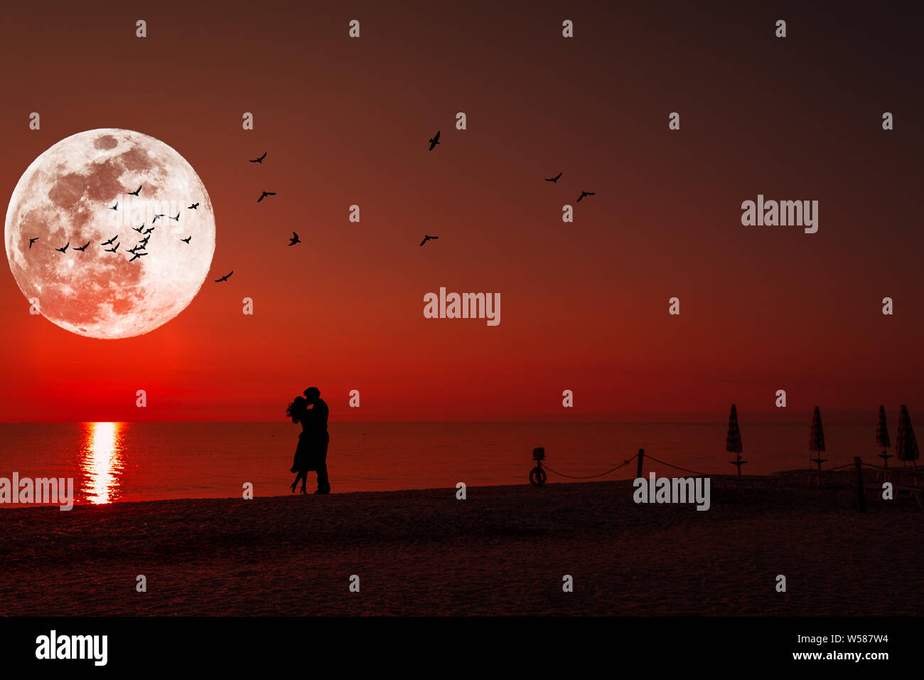 Silhouette of a kissing couple under full moon at sunset Stock Photo ...