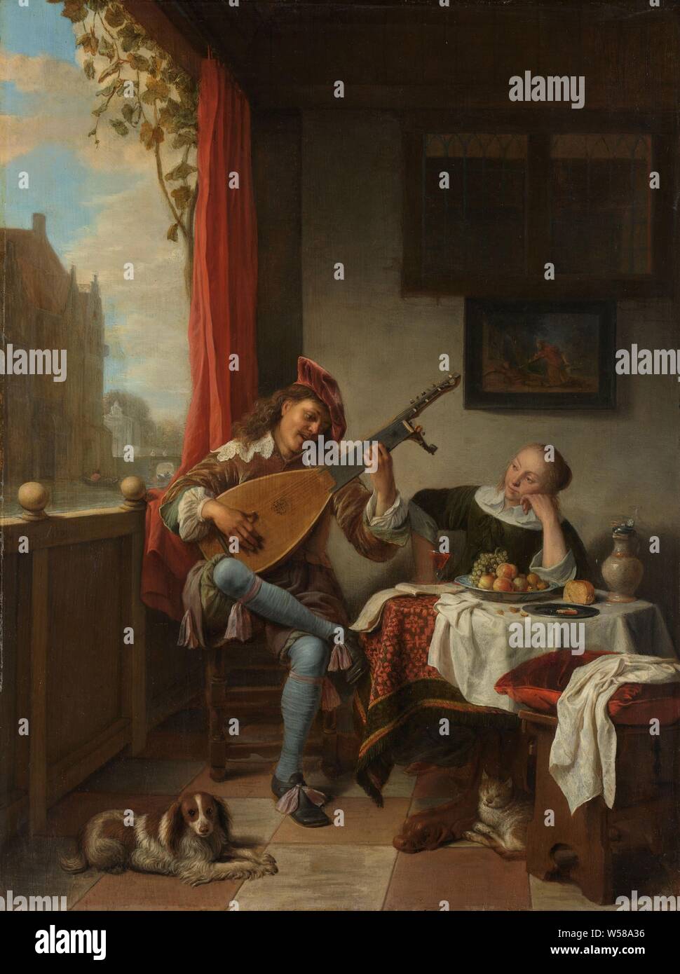 The Lutenist Lute Player, The Lute Player. In a room a young man plays on the lute for a woman sitting and listening at a table. On the table a bowl with fruit, bread, a jug and an open music book. On the floor a dog and a cat, on the wall is a painting of Pyramus and Thisbe., Hendrick Martensz. Sorgh, 1661, panel, oil paint (paint), h 51.5 cm × w 38.5 cm t 6 cm Stock Photo