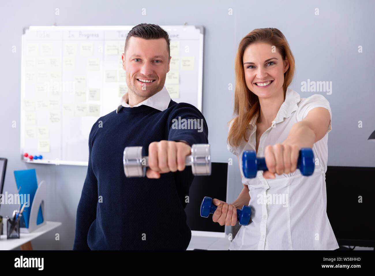 Close-up Of Male And Female Businesspeople Exercising In Office With Dumbbells Stock Photo