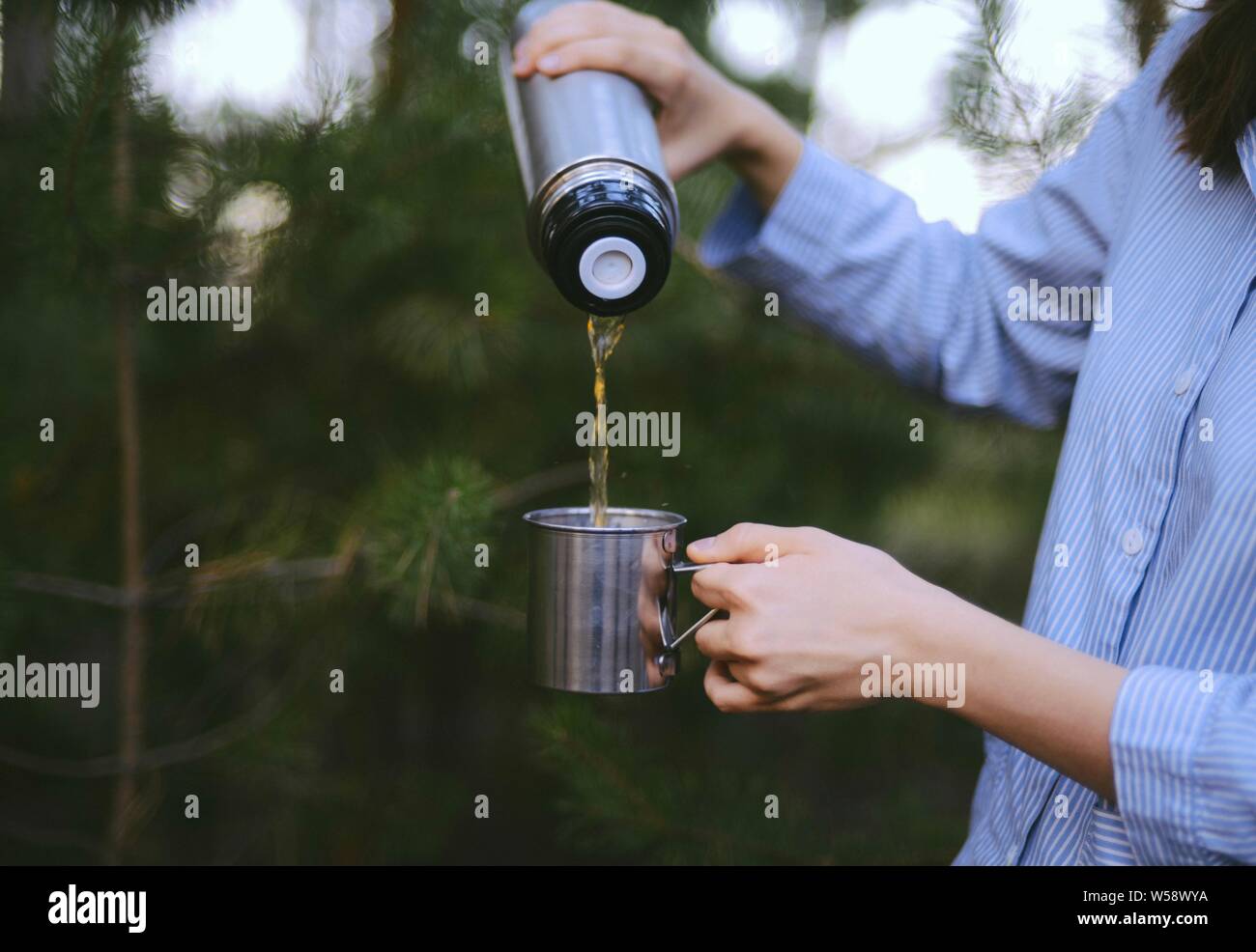 Woman is pouring hot drink from thermos into travel mug