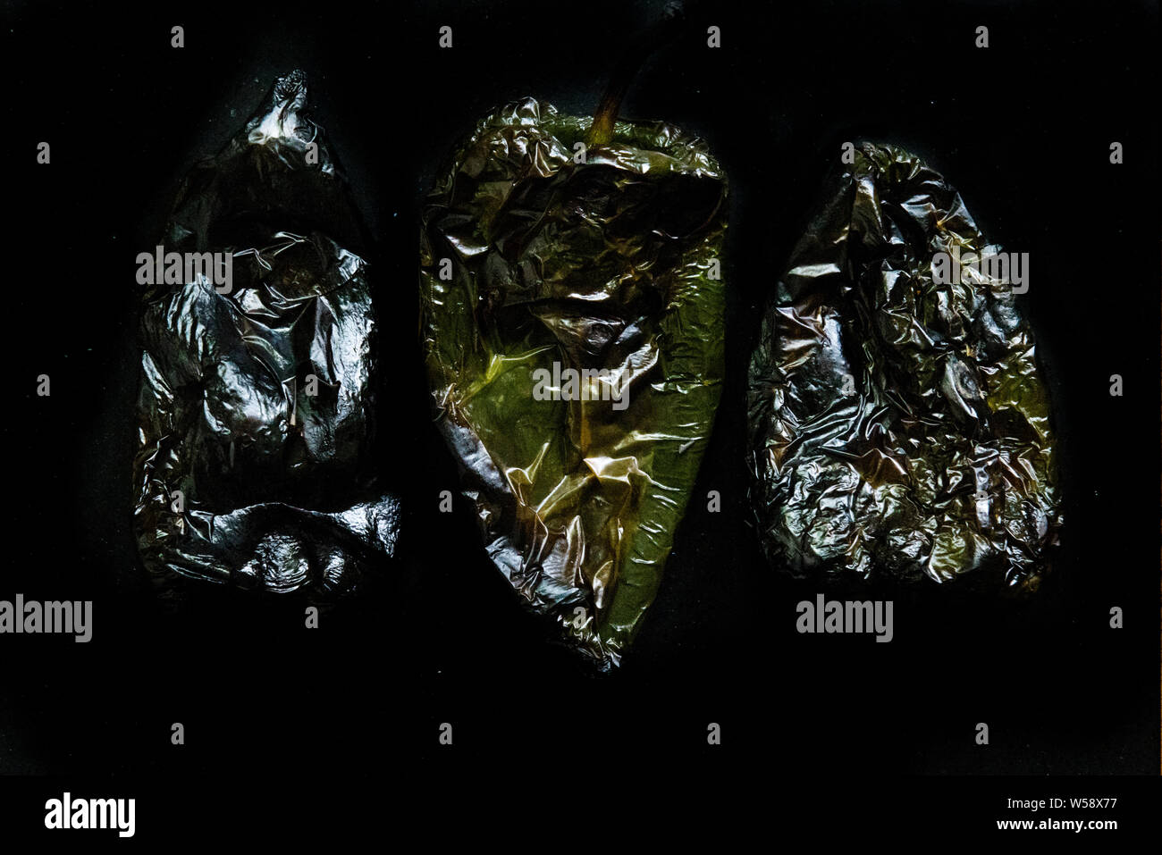 Three charred Poblano peppers against a black background Stock Photo