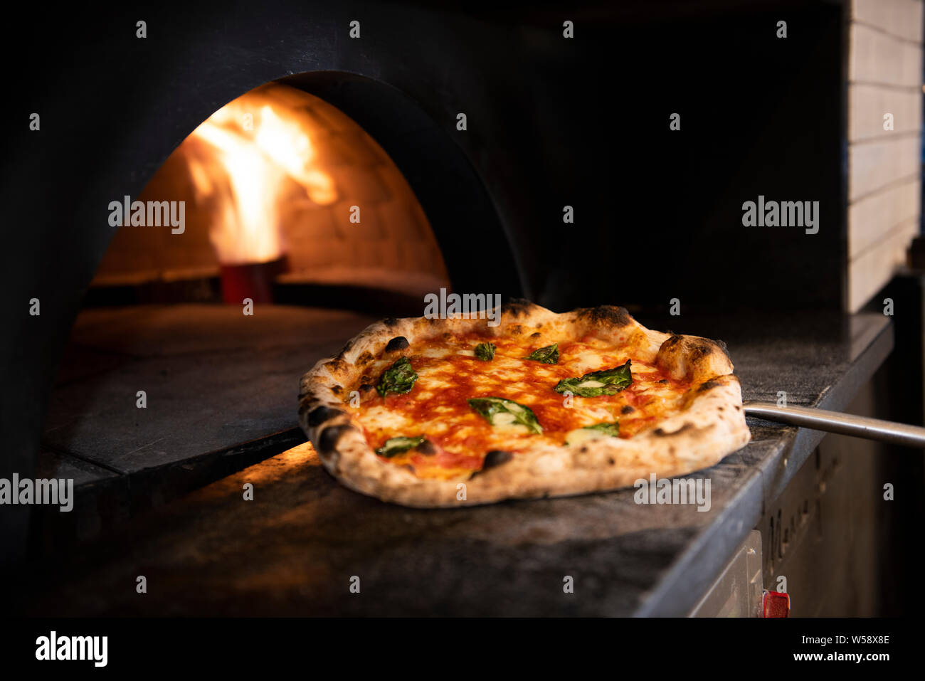 Thin-crust pizza out of wood-fired oven with flames in background Stock Photo