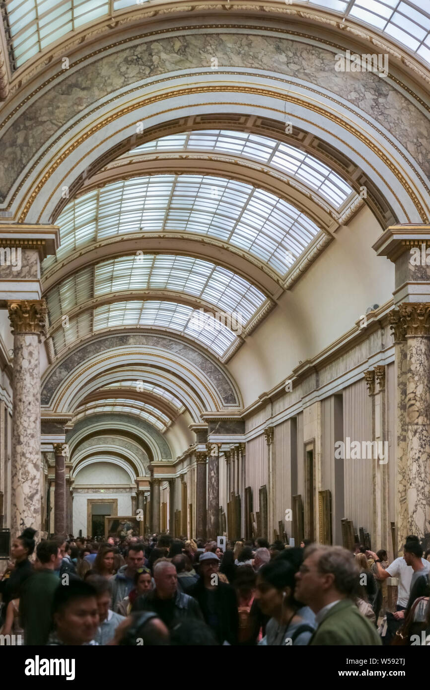 A visitor crowd walking at the art galleries of the famous and popular Louvre Museum and admiring the beautiful paintings. Stock Photo
