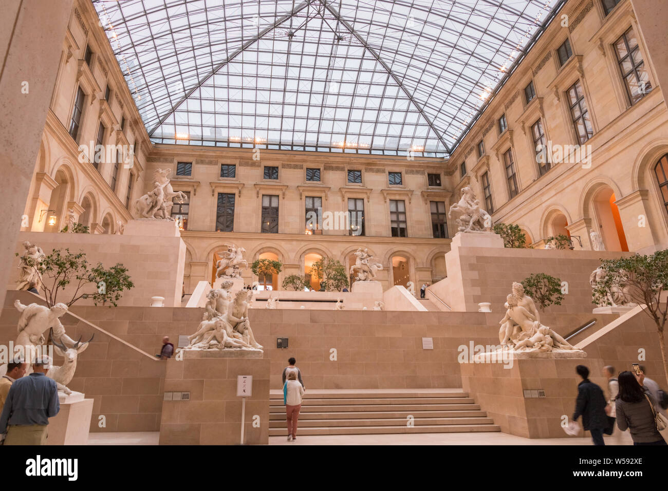 Panoramic low-angle view of the indoor sculpture garden Cour Marly in the Louvre’s Richelieu Wing. Visitors in the glass-roofed courtyard can admire... Stock Photo