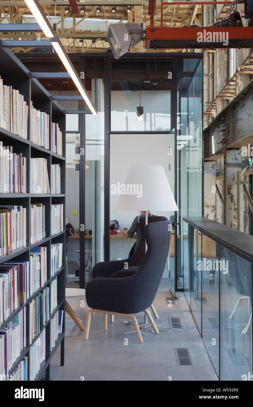 Bookshelves with study cubicle behind, and grey chair in foreground. Bibliotheek LocHal, Tilburg, Netherlands. Architect: CIVIC Architects / Braaksma Stock Photo
