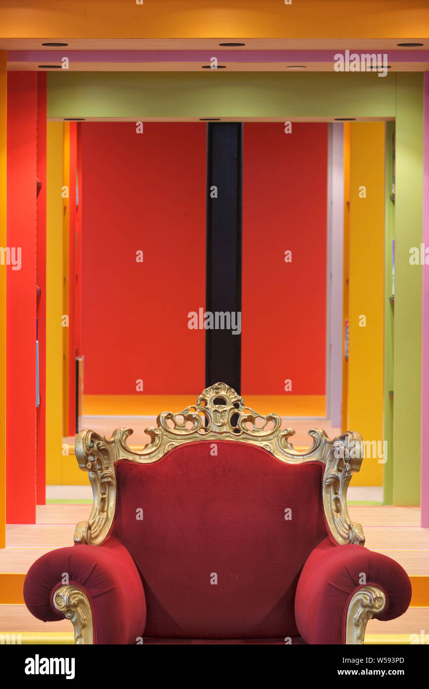 Red upholstered gilt throne in children's library, with fluorescent painted rectangular arches behind. Bibliotheek LocHal, Tilburg, Netherlands. Archi Stock Photo