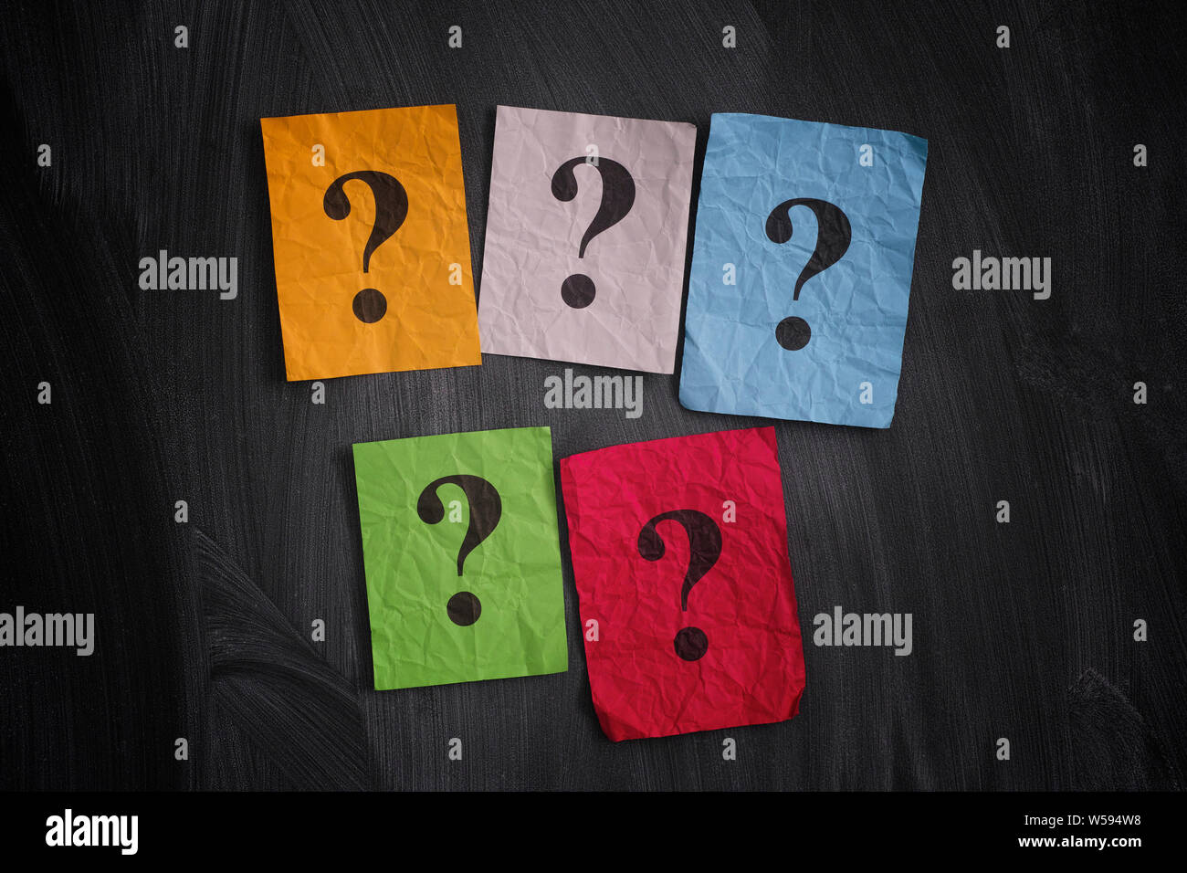 Colorful paper notes with question marks on black board. Close up. Stock Photo