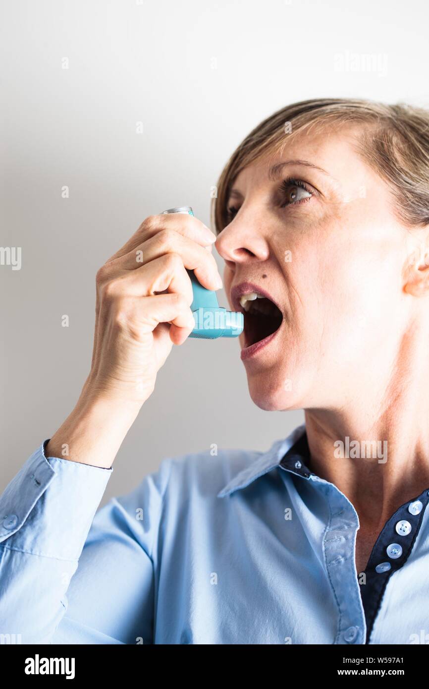 Woman using an inhaler to treat an asthma attack. The inhaler contains
