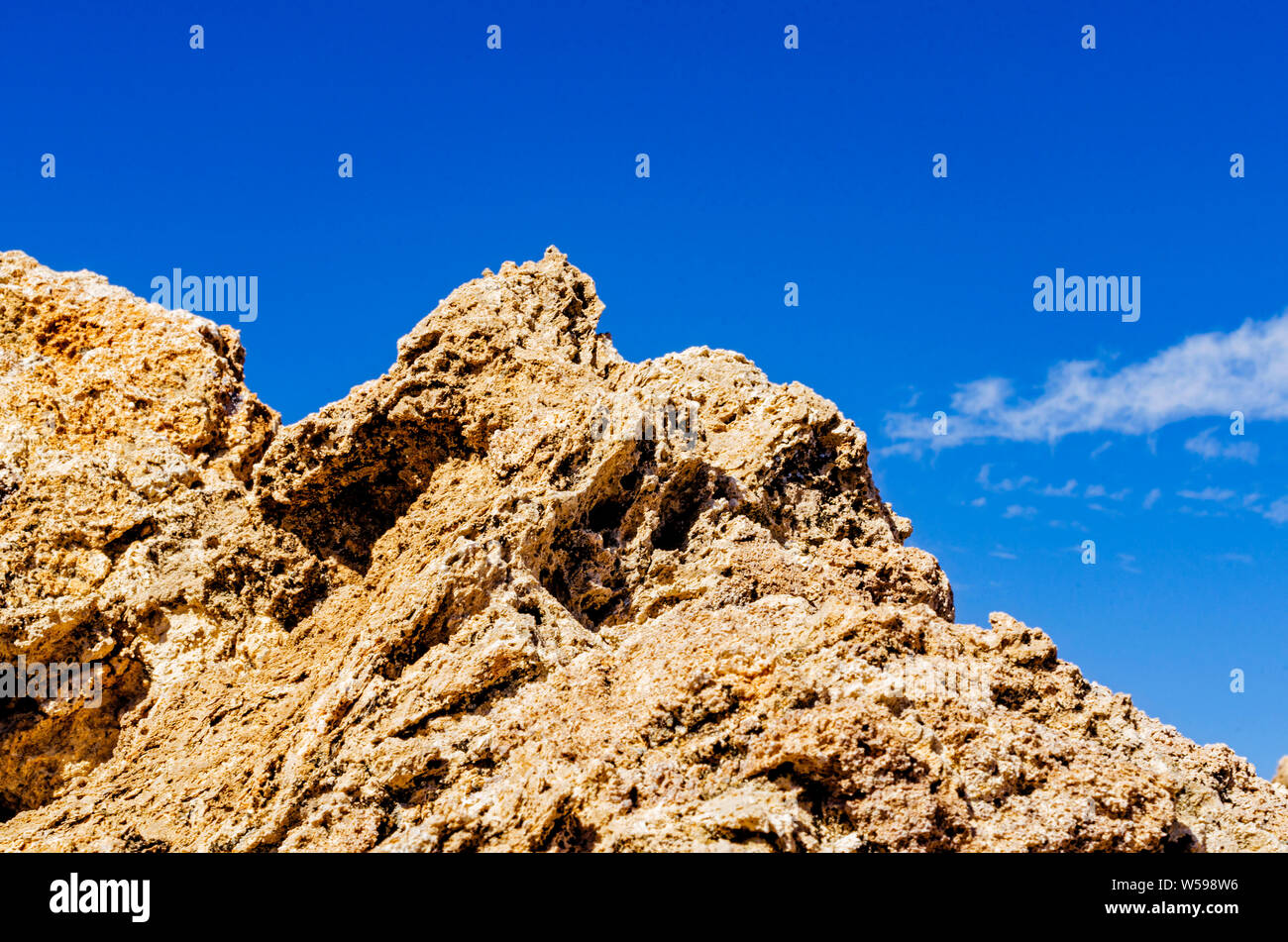 Rough jagged rocky peak against blue sky with white cloud. Stock Photo