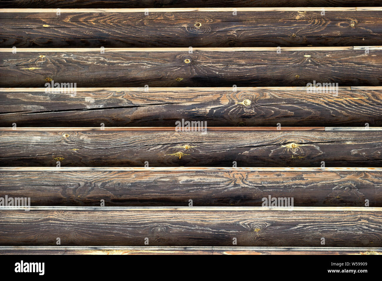 Wall from wooden logs. Background with copy space. Horizontal lines of dark brown weathered wood material. Place for custom text. Log house exterior. Stock Photo