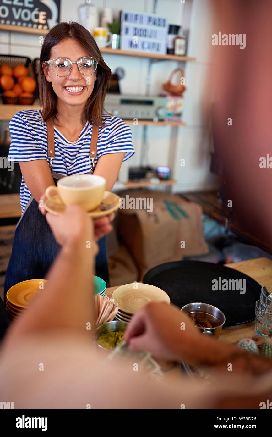 Smiling waitress in cafe serving customer with coffee. Stock Photo