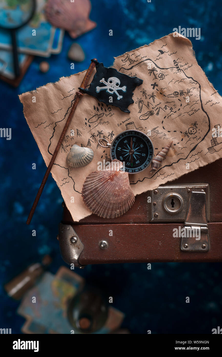 Treasure map with seashells and Jolly Roger on a suitcase. Ready to go for an adventure flat lay with copy space. Stock Photo