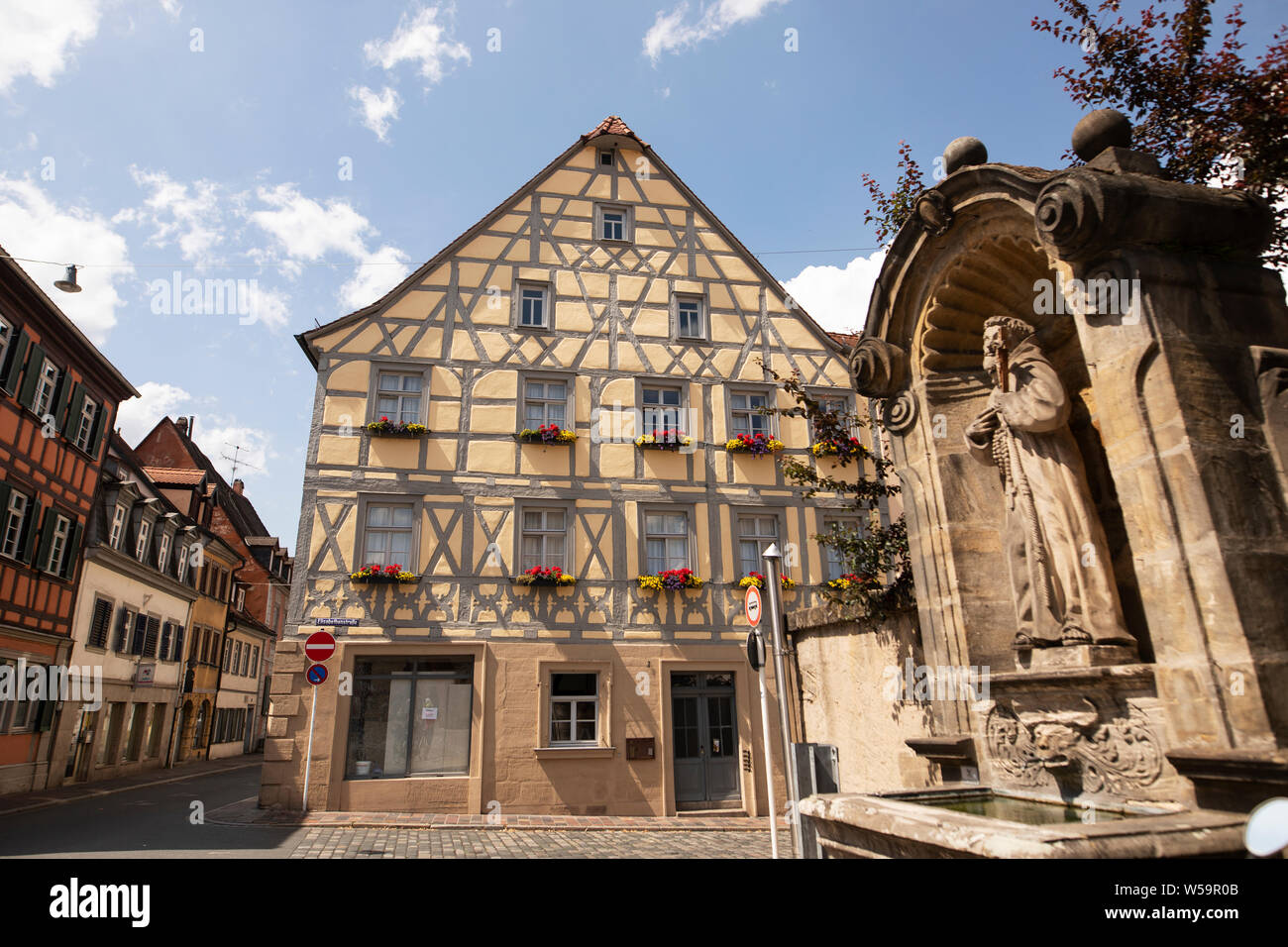 A traditional house (Bauernhaus or farmhouse) and the water fountain outside the Elisabethenkirche in the Bavarian city of Bamberg, Germany. Stock Photo