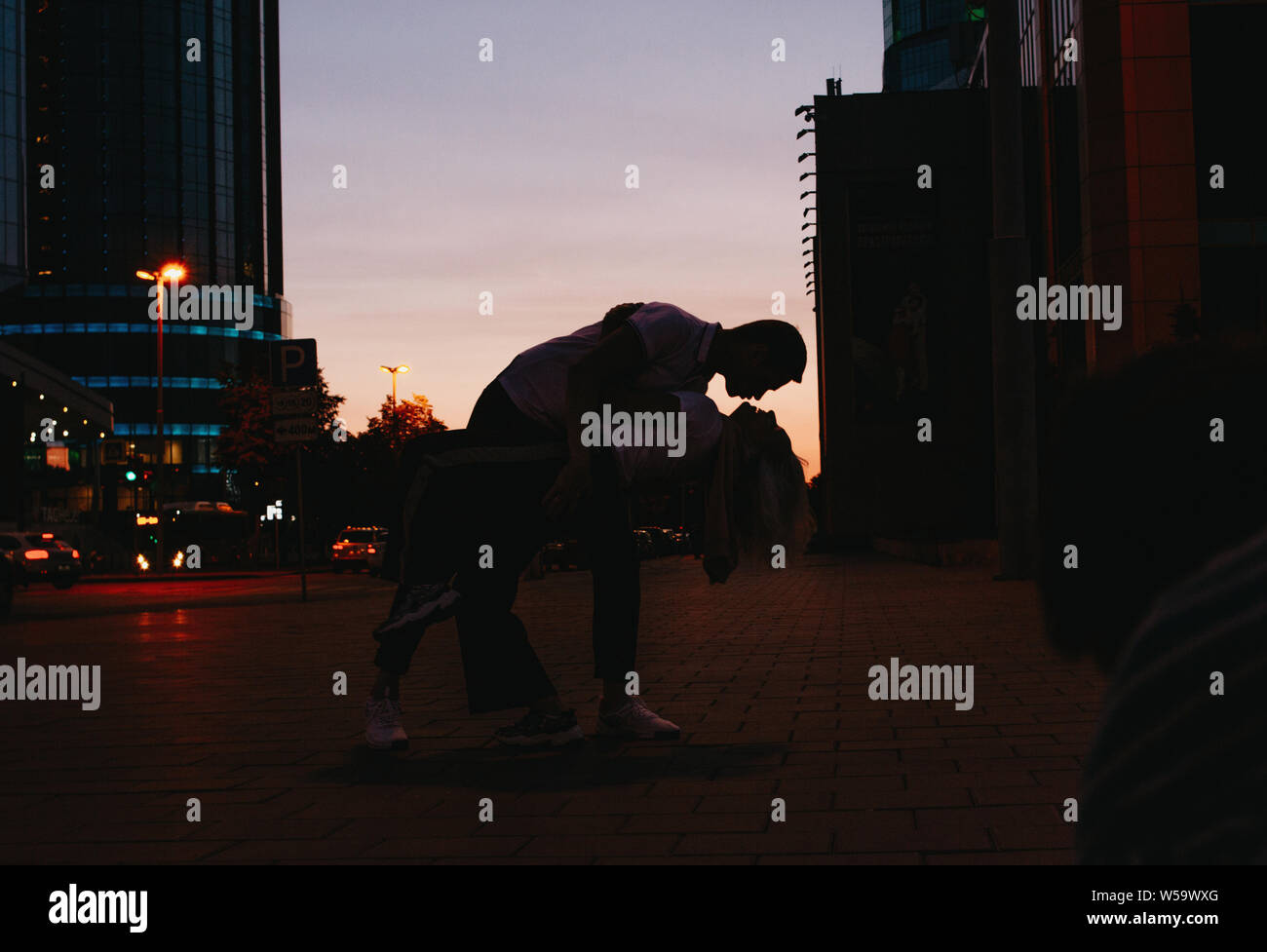 Silhouette of young happy couple in love dancing on city street at the ...