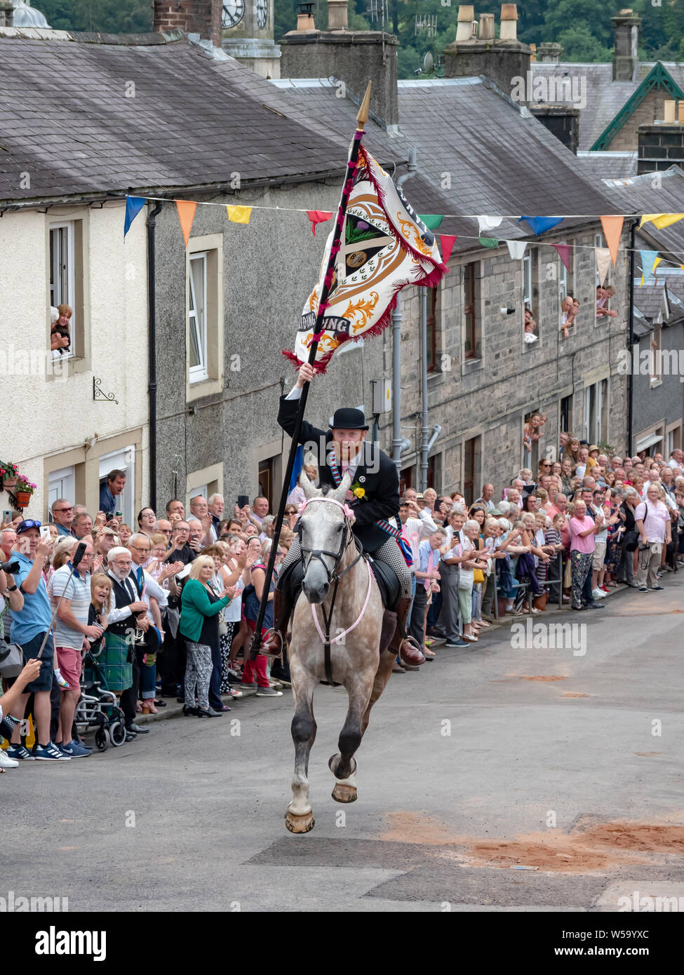 Langholm, Dumfries and Galloway, Scotland, UK. 26th July 2019. The Cornet, Henry Jeffrey, gallops up the Kirk Wynd carrying the Common Riding flag. Stock Photo