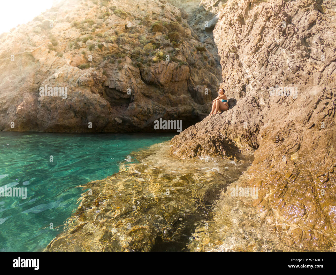 Beautiful young woman sitting on a cliff rock under the summer sun in swimswear on ponza island tanning Stock Photo