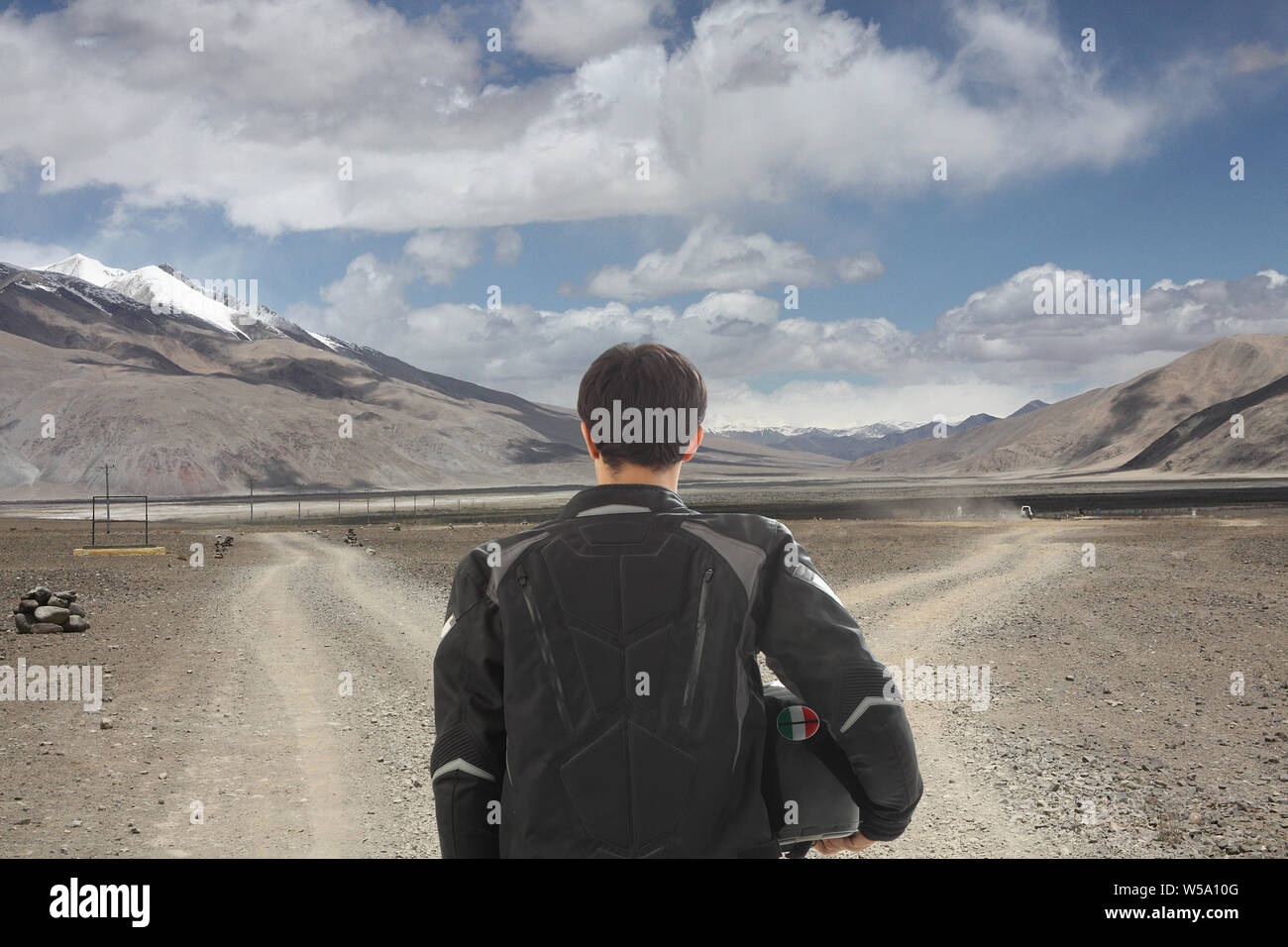 Rear view of biker standing at fork in dirt road, Ladakh, Jammu and Kashmir, India Stock Photo