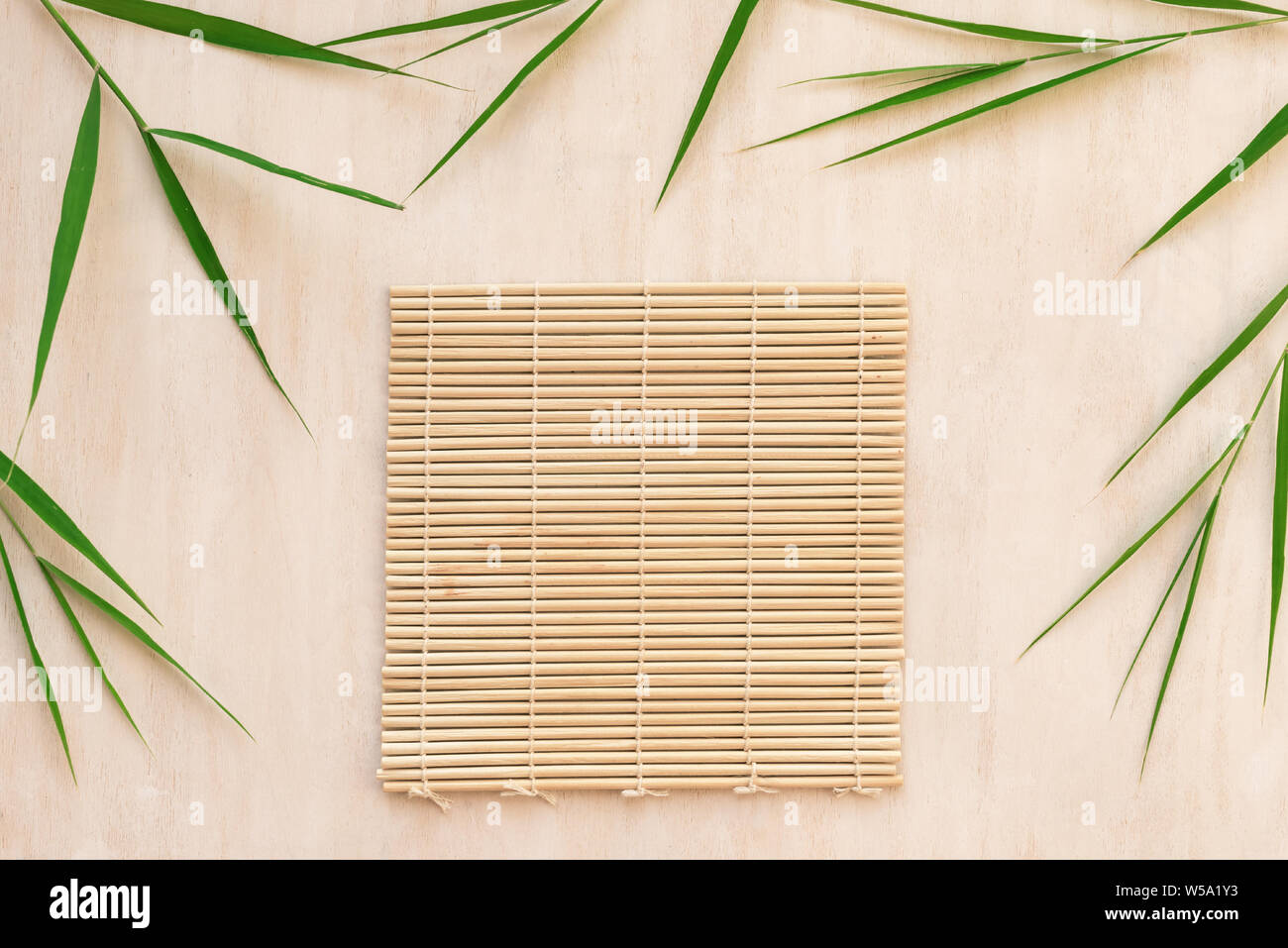 Green bamboo leaves and bamboo mat, asian style background, top view, copy space. Trendy bamboo leaves flat lay on white wooden background. Stock Photo