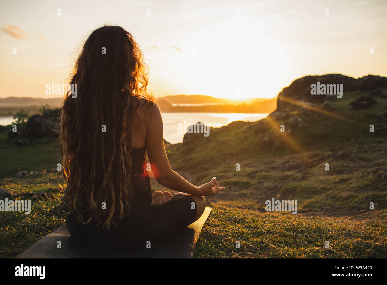 Woman meditating yoga alone at sunrise mountains. View from behind. Travel Lifestyle spiritual relaxation concept. Harmony with nature. Stock Photo