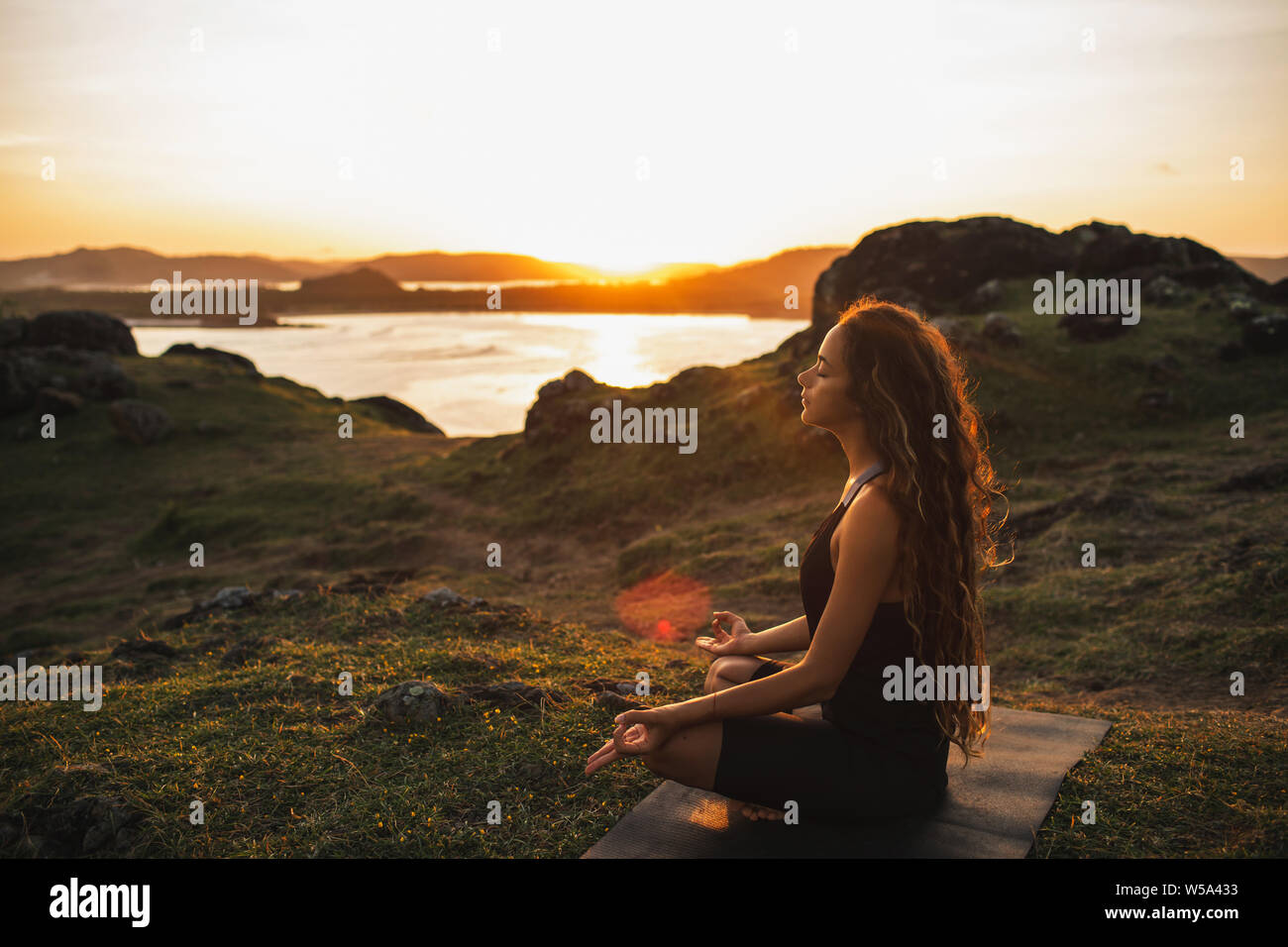 Woman doing yoga alone at sunrise with mountain and ocean view. Harmony with nature. Self-analysis and soul-searching Stock Photo
