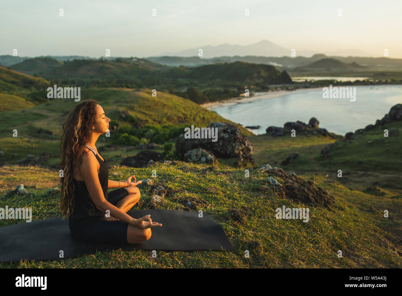 Woman doing yoga alone at sunrise with mountain and ocean view. Harmony with nature. Self-analysis and soul-searching Stock Photo