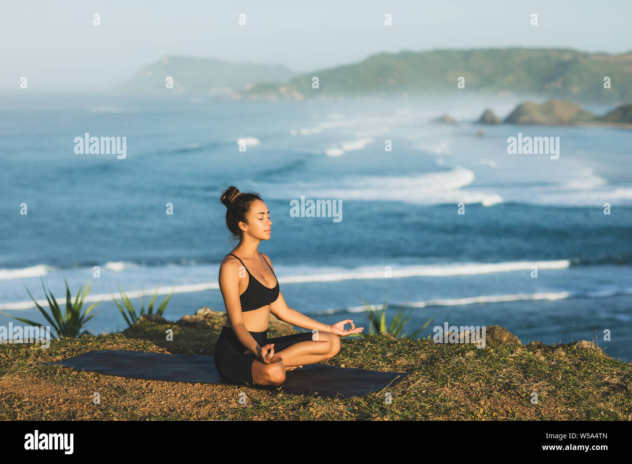 Woman practicing yoga and sitting in lotus pose outdoor with amazing ocean view. Health and well-being concept. nature background. Stock Photo