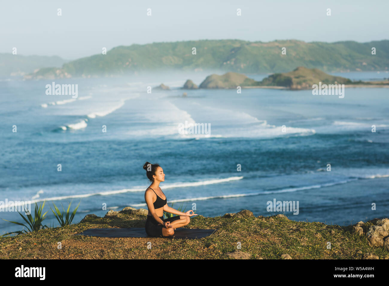Woman practicing yoga and sitting in lotus pose outdoor with amazing ocean view. Health and well-being concept. nature background. Stock Photo